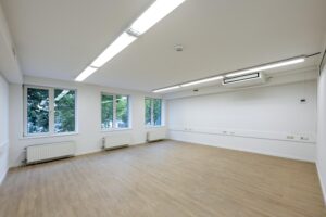 Leeg kantoorruimte met houten vloer, witte muren, grote ramen en ingebouwde verlichting aan de Prins Hendrikkade.